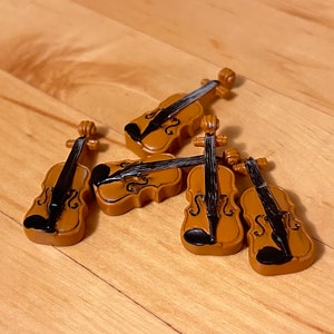 Peut inclure: Cinq violons miniatures en bois avec des cordes noires et de la peinture brune. Les violons sont disposés en grappe sur une surface en bois.