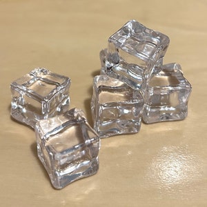 May include: Five clear plastic ice cubes on a light brown wooden surface.
