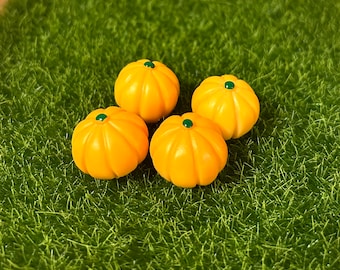 Puede incluir: Cuatro calabazas naranja en miniatura con tallos verdes, dispuestas sobre un lecho de hierba artificial verde.