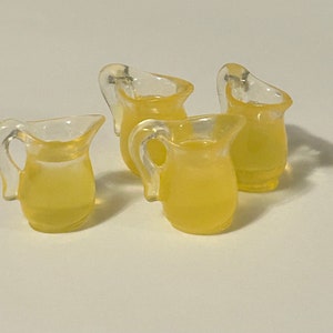 May include: Four small, clear glass pitchers filled with a yellow liquid. The pitchers have a rounded body and a handle.
