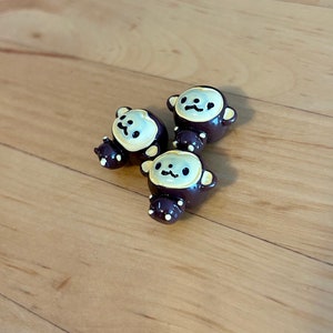 May include: Three small ceramic monkey figurines with brown bodies and yellow faces. The monkeys have black eyes and are looking in different directions.