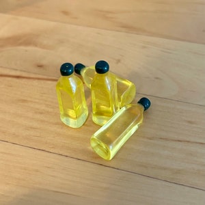Peut inclure: Quatre bouteilles en verre miniatures avec des bouchons noirs remplies d'un liquide jaune. Les bouteilles sont disposées sur une surface en bois brun clair.