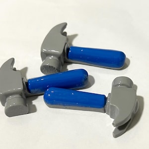 May include: Three miniature toy hammers with blue handles. The hammers are made of grey plastic and have a rounded head.