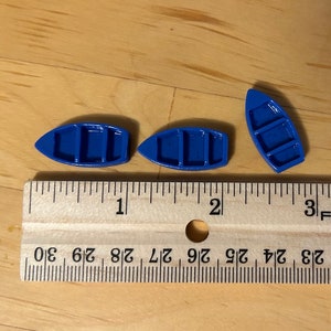 May include: Three small blue toy boats, each with three rows of holes, are lined up on a wooden ruler. The ruler is marked with inches and fractions of an inch.