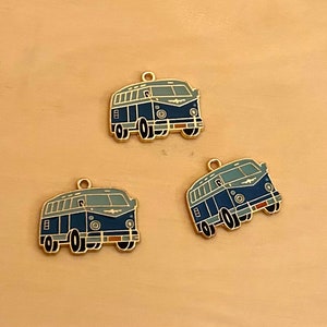 May include: Three gold-coloured charms shaped like blue and grey vintage vans. Each charm has a loop at the top for attaching to a necklace or bracelet.