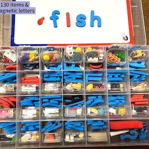 Puede incluir: Un contenedor de almacenamiento de pl&aacute;stico transparente con m&uacute;ltiples compartimentos llenos de peque&ntilde;os objetos coloridos y letras magn&eacute;ticas. La tapa blanca muestra el texto 130 items & magnetic letters y la palabra fish.