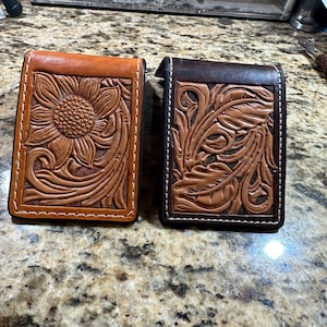 May include: Two leather wallets with tooled designs. One wallet is brown with a sunflower design and the other is black with a floral design.