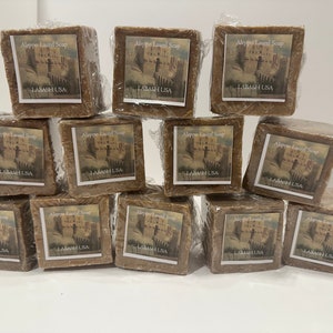 Puede incluir: Una pila de 12 barras marrones de jab&oacute;n de laurel de Alepo, cada una envuelta en pl&aacute;stico y etiquetada con el texto "Aleppo Laurel Soap" y "LABASH USA".