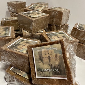 Puede incluir: Una pila de barras de jab&oacute;n de laurel de Alepo marrones envueltas en pl&aacute;stico. Las barras de jab&oacute;n est&aacute;n etiquetadas con el texto "Aleppo Laurel Soap" y "Labash USA".