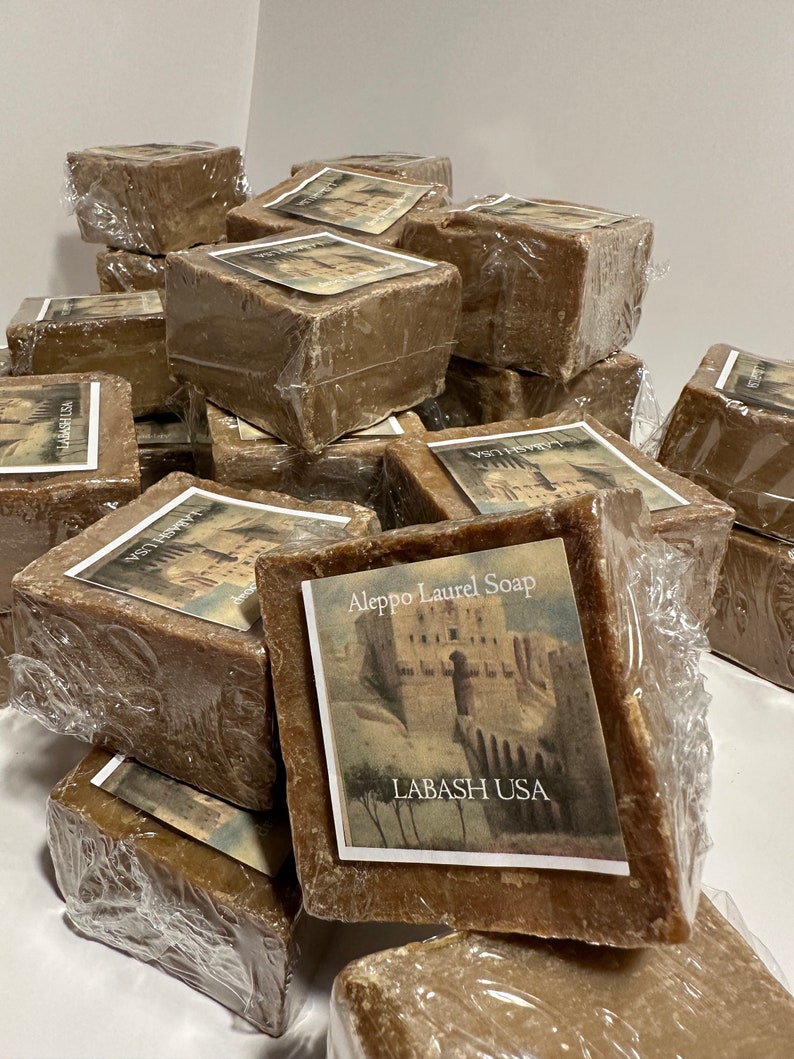 Puede incluir: Una pila de barras de jab&oacute;n de laurel de Alepo marrones envueltas en pl&aacute;stico. Las barras de jab&oacute;n est&aacute;n etiquetadas con el texto "Aleppo Laurel Soap" y "Labash USA".