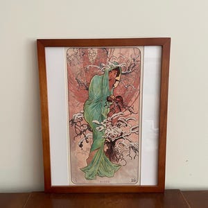 May include: A framed print of a woman in a green gown standing in a snowy forest. The print is titled "HIVER" which is French for "Winter".