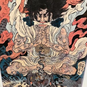 May include: A detailed Japanese woodblock print featuring a seated figure with a stern expression, dark hair, and a white robe. The artwork includes a snake, a turtle, and various mythical creatures, with red, blue, and gold accents.