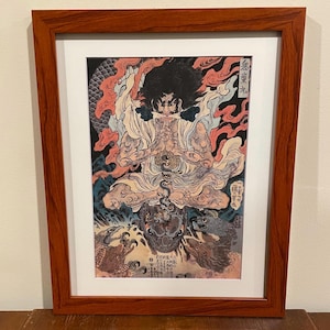May include: Framed Japanese woodblock print featuring a seated figure with a fierce expression, surrounded by flames and mythical creatures. The artwork is in a wooden frame with a white mat.