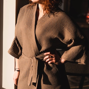 May include: A brown waffle weave robe with a tie belt. The robe is made of a soft, comfortable material and has a relaxed fit.