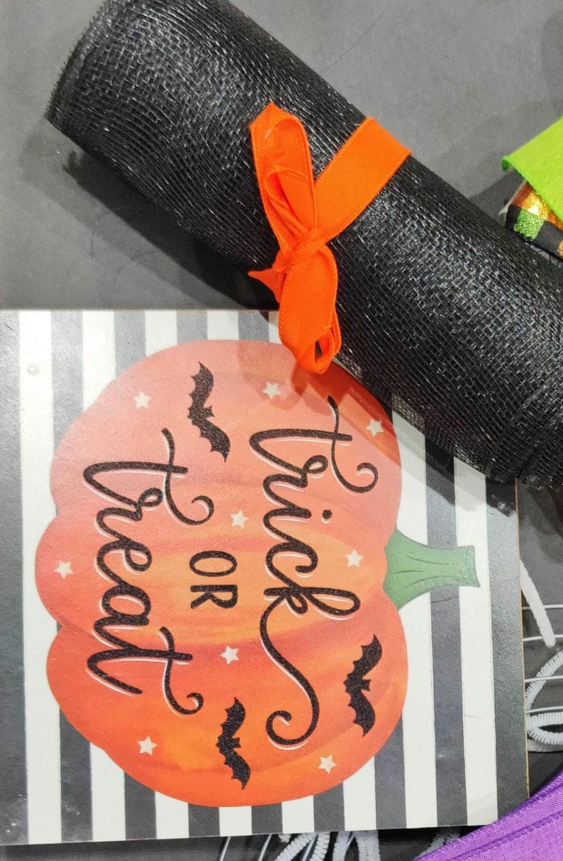 May include: A black and white striped pumpkin with the text "Trick or Treat" in black script. There are black bats flying around the pumpkin. The pumpkin is on a wooden sign with a black and white striped background.
