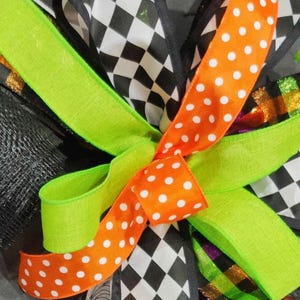 May include: A Halloween wreath with a black and white checkered ribbon, a green ribbon with orange polka dots, and a multi-colored ribbon with a glittery purple stripe.
