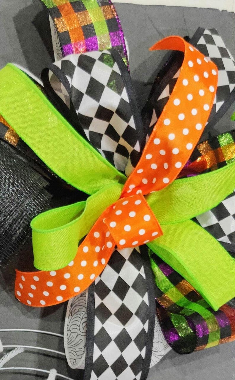 May include: A Halloween wreath with a black and white checkered ribbon, a green ribbon with orange polka dots, and a multi-colored ribbon with a glittery purple stripe.