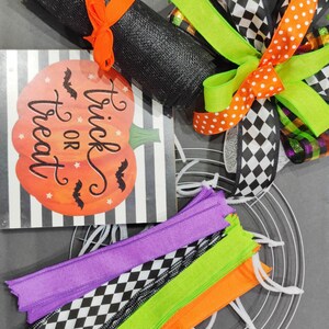 May include: Halloween wreath making kit with black mesh, orange and white polka dot ribbon, black and white checkered ribbon, green ribbon, purple, green, orange and black and white checkered ribbon, a metal wreath form, and a sign that says "Trick or Treat".