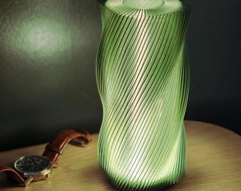 May include: A green, 3D printed lamp with a spiral design. The lamp is turned on and casting a warm glow.
