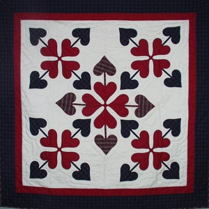 May include: A white quilt with a red, white and blue patchwork design. The quilt features a repeating pattern of hearts and arrows.