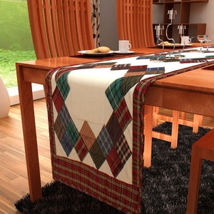 May include: A plaid table runner with a white background and a red, green, and blue plaid border. The runner is on a wooden table with two chairs and a black rug.