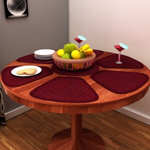 Op de afbeelding: Een ronde houten tafel met zes donkerrode placemats in een cirkel gerangschikt. Een kom met fruit staat in het midden van de tafel, omringd door twee glazen met cocktailparasols.