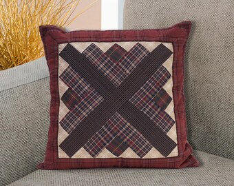 Puede incluir: Una almohada de color rojo, marrón y blanco a cuadros con un gran diseño en forma de X marrón. La almohada está sentada en un sofá gris claro.