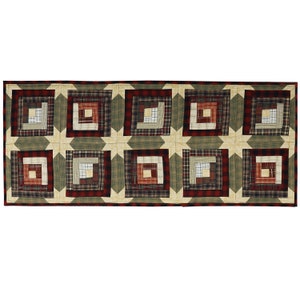 May include: A long rectangular table runner with a patchwork design featuring a log cabin pattern in shades of red, green, and brown.