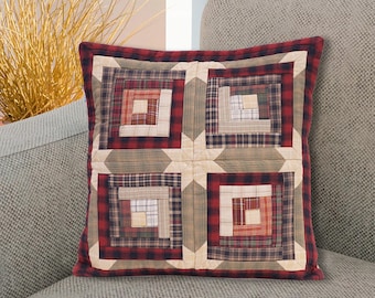 Puede incluir: Una almohada de color rojo y verde a cuadros con un patrón de edredón de cabaña de troncos. La almohada está sentada en un sofá gris.