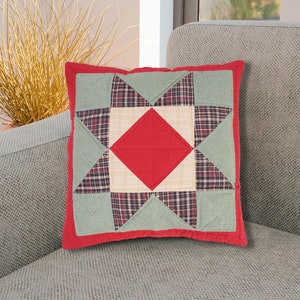 Puede incluir: Una almohada de patchwork roja, verde y crema con un diseño de estrella. La almohada está sentada en un sofá gris.