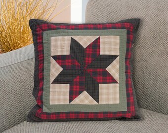 Puede incluir: Una almohada de tiro de cuadros rojos, negros y verdes con un diseño de estrella. La almohada está sentada en un sofá gris.