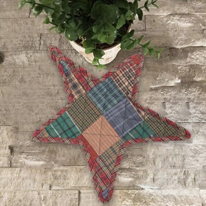 Op de afbeelding: Een stervormige ovenwant in patchwork met rode, groene, blauwe en bruine ruitjespatronen. De ovenwant is gemaakt van gestikt stof en heeft een bruine rand.