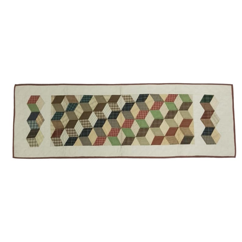 May include: A rectangular quilted table runner with a repeating geometric pattern of 3D cubes in various colors, including red, green, brown, and cream. The runner has a cream-colored border with a brown trim.