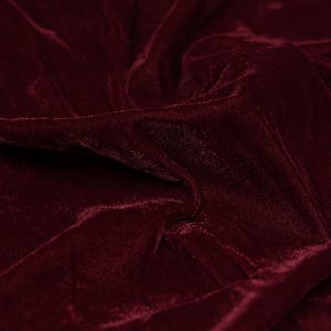 May include: Close-up of a deep red velvet fabric with a soft, plush texture. The fabric is draped and folded, creating a luxurious and elegant look.