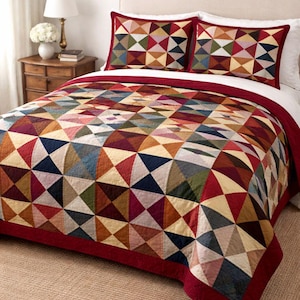 May include: A bed is made with a colourful quilt and two matching pillow shams. The quilt and shams feature a geometric pattern of triangles in shades of red, blue, green, and tan. The quilt has a red border and is on a bed with white sheets.