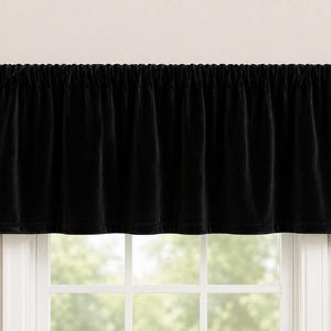 May include: A solid black velvet window valance featuring a rod pocket header that creates soft, vertical gathers across the fabric. The valance is suspended on a dark metal curtain rod with spherical finials, providing a clean, uniform drape.