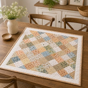 Peut inclure: Chemin de table matelassé carré avec un motif floral dans les tons orange, jaune, vert et bleu. Le chemin de table a une bordure blanche et est posé sur une table en bois. La table est ornée d'un vase de fleurs et d'un petit bol en bois.