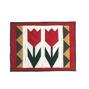 May include: A red and green quilted throw pillow with a design of two tulips. The pillow has a white background and a red, green, and brown border.