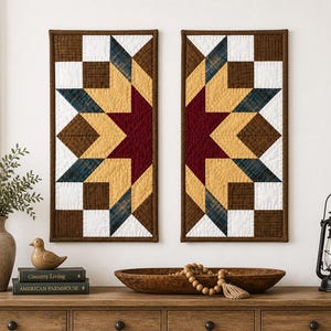 May include: Two rectangular wall hangings with a star pattern. Each features a burgundy star in the center, surrounded by yellow, blue, white, and brown geometric shapes. The borders are a dark brown, and the overall style is rustic.