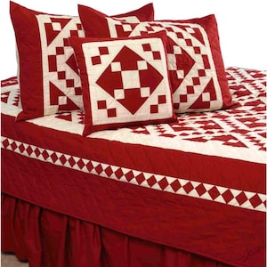 Op de afbeelding: Een rood-witte quiltset met bijpassende kussenslopen. De quilt en kussenslopen hebben een geometrisch patroon van rode vierkanten en ruiten op een witte achtergrond. De bedrok is effen rood.
