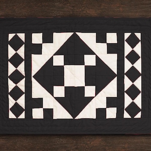 May include: Black and white quilt with a geometric pattern. The quilt is made of squares and triangles and has a black border.