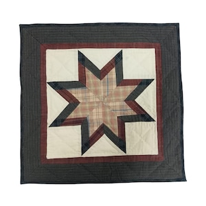 May include: Square quilted pillow with a star design. The star features a plaid pattern in shades of red, cream, and blue. The star is set against a cream background, framed by a red border and a dark gray plaid outer border.
