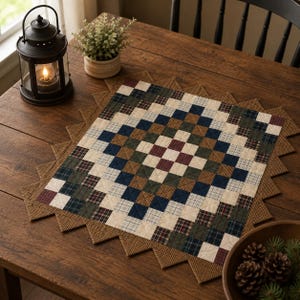 May include: A quilted table runner with a patchwork design in shades of blue, green, brown, and cream. The runner has a sawtooth edge and is placed on a wooden table. A lit lantern and potted plant are in the background.