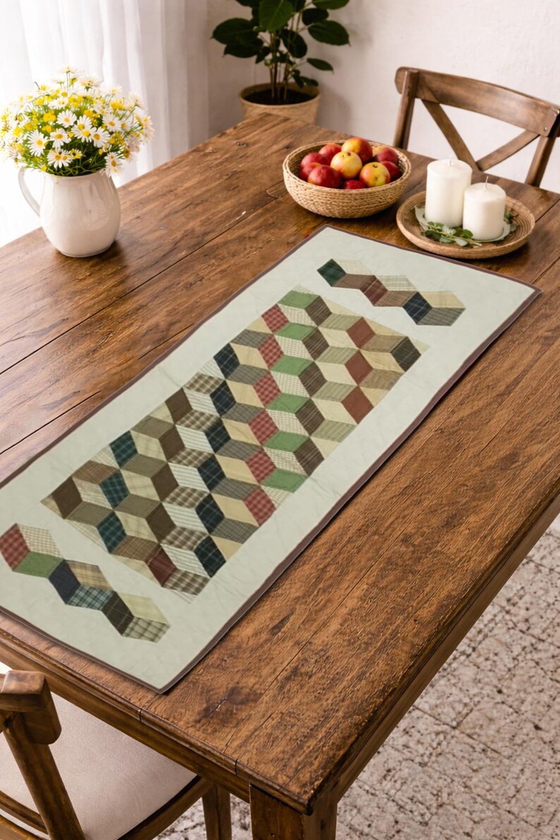 May include: A rectangular table runner with a geometric cube pattern in shades of brown, green, and red. The runner is placed on a wooden table, with a vase of flowers and a bowl of fruit nearby. The runner is approximately 12 inches wide.
