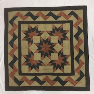 May include: A brown, tan, and red quilt with a starburst pattern in the center and a geometric border.