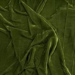 Könnte beinhalten: Olivgrüner Samtstoff mit weicher, glänzender Textur. Der Stoff ist drapiert und erzeugt Falten und Schatten, die sein weiches Aussehen hervorheben. Die Farbe ist ein sattes, tiefes Grün, geeignet für Kleidung oder Heimdekoration.