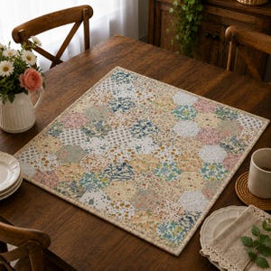 Peut inclure: Un tapis en tissu carré présentant un motif patchwork composé de divers imprimés floraux dans des tons de rose, bleu, jaune et blanc. Le tapis est constitué de pièces de tissu hexagonales assemblées avec une bordure de couleur claire.