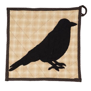 May include: Square quilted pot holder featuring a black crow silhouette on a beige plaid background. The pot holder has a brown border and a loop for hanging. The crow is detailed with textured fabric.