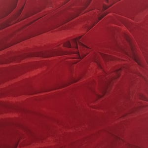 Pode incluir: Um close-up de um tecido de veludo vermelho profundo. O material é drapeado e dobrado, criando sombras e destaques que enfatizam sua textura macia. A cor rica e o brilho sugerem um têxtil de alta qualidade.