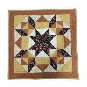 Può includere: Trapunta quadrata con motivo a stella. La trapunta presenta un motivo a stella centrale con stampa floreale, circondato da forme geometriche nei toni del marrone, beige e bianco. Il bordo è marrone pieno e i bordi sono rifiniti con un bordo in corda beige.